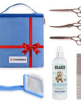 Blue organizer bag sits beside three bronze scissors a long tooth metal comb a blue handled slicker brush and a white detangler spray bottle.