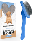 Blue slicker brush with long bent metal pins and a curved ergonomic handle positioned beside a white We Love Doodles retail box that shows a puppy and the large size label.