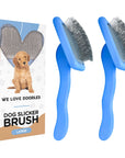 On a white background two large blue slicker brushes with bent stainless pins sit beside a branded We Love Doodles box with a puppy graphic.