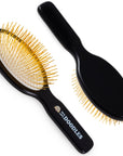 Black oval pin brush shown from front and back on a white background. Gold colored pins and a smooth black beechwood handle with logo are visible.
