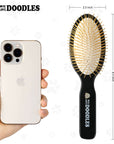 Black oval pin brush displayed next to a smartphone with measurements shown as about 8.5 inches long and 2.5 inches wide. Logo printed on the handle.