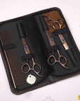 Brown zip case opened to display straight, curved, and thinning scissors with a metal comb on a light surface with paw prints.