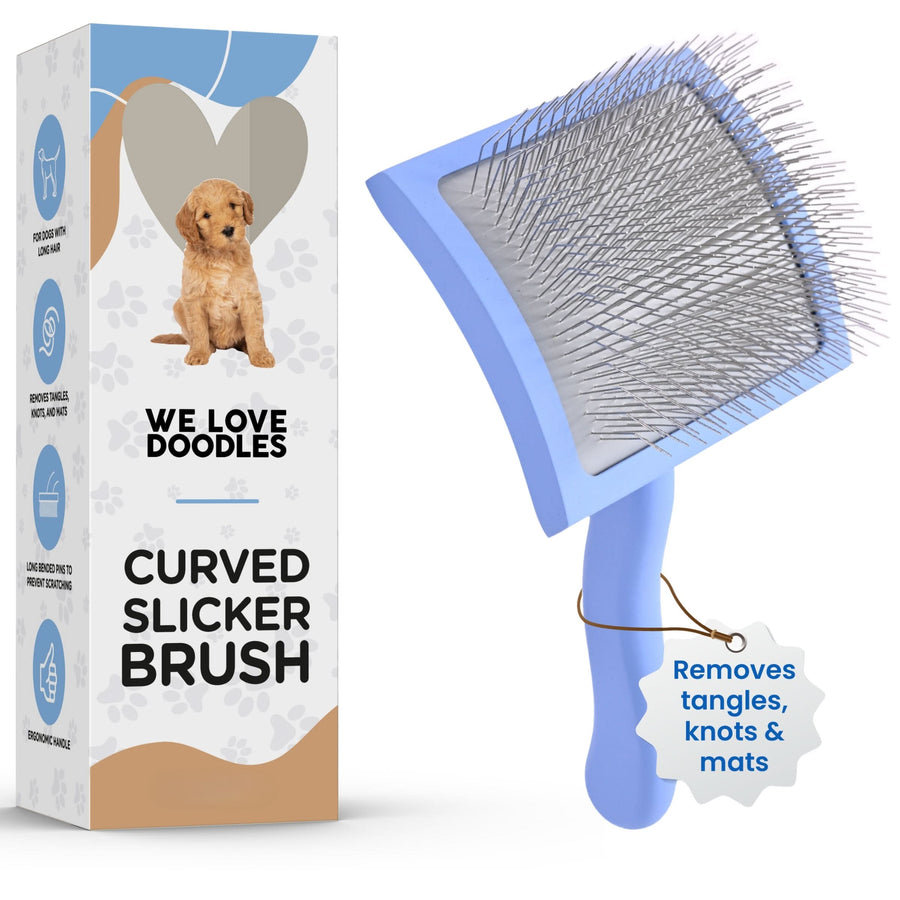 Light blue curved slicker brush with dense stainless steel pins shown beside a We Love Doodles box. A small tag on the handle reads removes tangles, knots and mats.