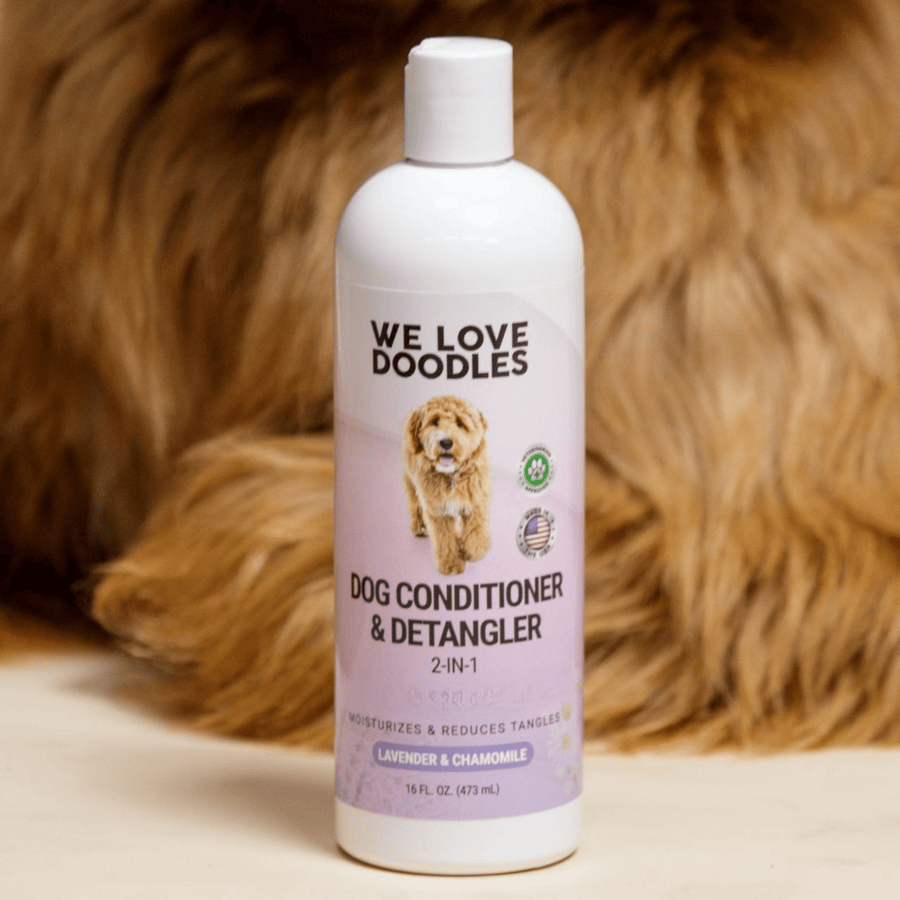 The We Love Doodles conditioner stands upright on a light surface with curly brown dog fur filling the background. The purple label and logo are clear and readable.