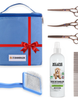 Blue handled slicker brush, white detangler bottle, metal comb, and three bronze scissors laid beside a blue zip bag with a red bow and carry handle.