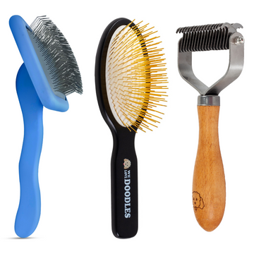 Blue slicker brush with bent pins, black pin brush with gold pins, and a wood handle dematting rake with metal blades on a white background.