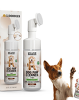 White foam dog paw cleaner with built in brush stands beside its retail box. A brown and white dog raises a paw while a hand holds the bottle, ready to clean.