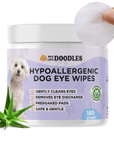 White plastic jar with a purple label that reads Hypoallergenic Dog Eye Wipes 150 count. A hand holds a textured round pad above the lid and an aloe plant is placed in front of the jar.