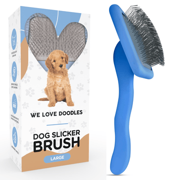 Blue slicker brush with long bent metal pins and a curved ergonomic handle positioned beside a white We Love Doodles retail box that shows a puppy and the large size label.
