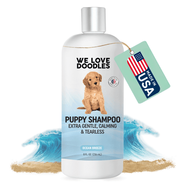 White 8 fl oz bottle labeled Puppy Shampoo extra gentle calming and tearless. A tan puppy is on the label. Waves and sand sit behind the bottle and a mint tag reads Made in USA.