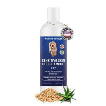 White bottle with a blue label reading Sensitive Skin Dog Shampoo 3 in 1. A Made in USA tag hangs at the neck. Oat flakes and aloe leaves sit at the base on a white background.