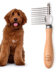 Fluffy brown dog sits next to a small dematting rake with nine stainless steel blades and a smooth wood handle on a white background.