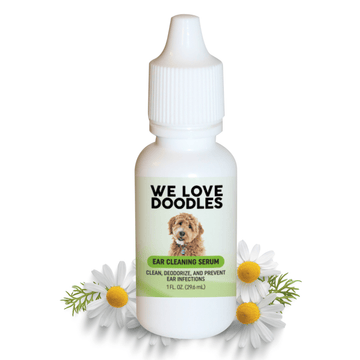 White 1 oz dropper bottle labeled We Love Doodles Ear Cleaning Serum with a doodle dog image and green label. Chamomile daisies sit around the bottle on a white background.