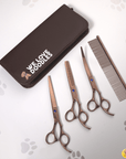 Three rose gold grooming scissors and a metal comb placed next to a closed brown case with We Love Doodles logo.
