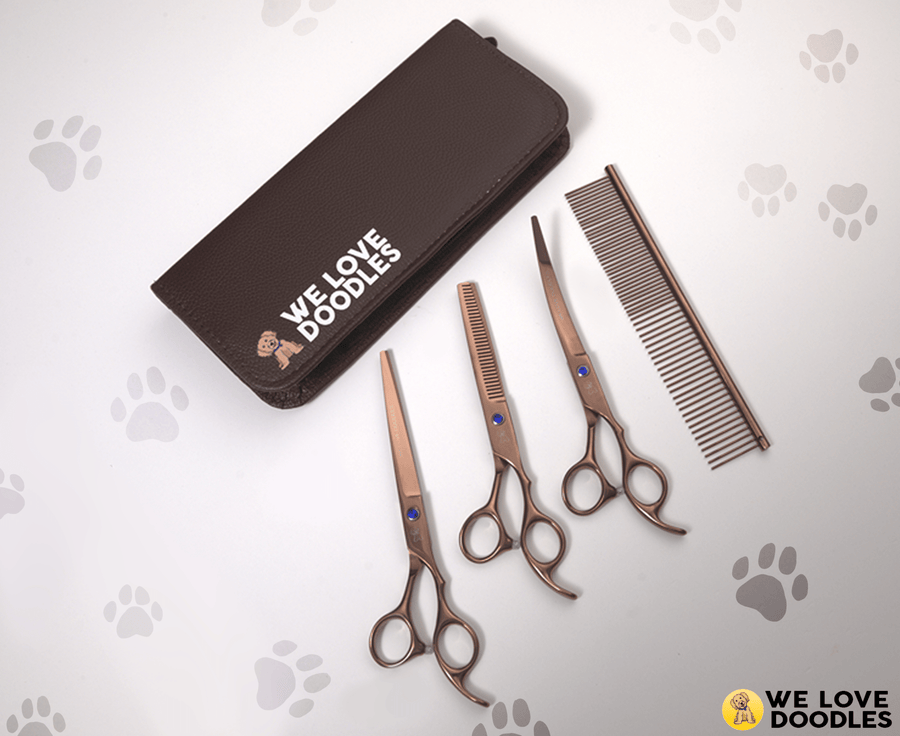 Three rose gold grooming scissors and a metal comb placed next to a closed brown case with We Love Doodles logo.
